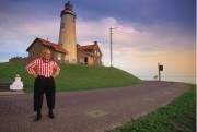 Netherlands, Urk. Senior fisherman in traditional clothing posing in front of a lighthouse. His wife is at the background.