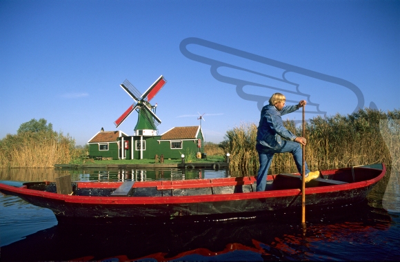 Man in a rowing boat passing a small windmill