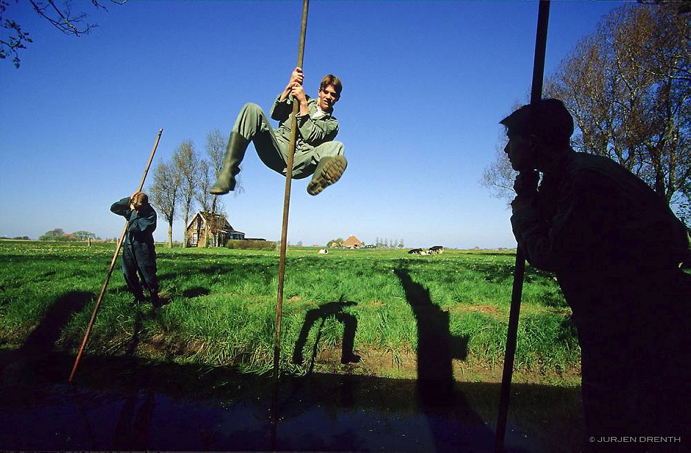 NETHERLANDS. FRIESLAND. BOYS LEAPING A DITCH